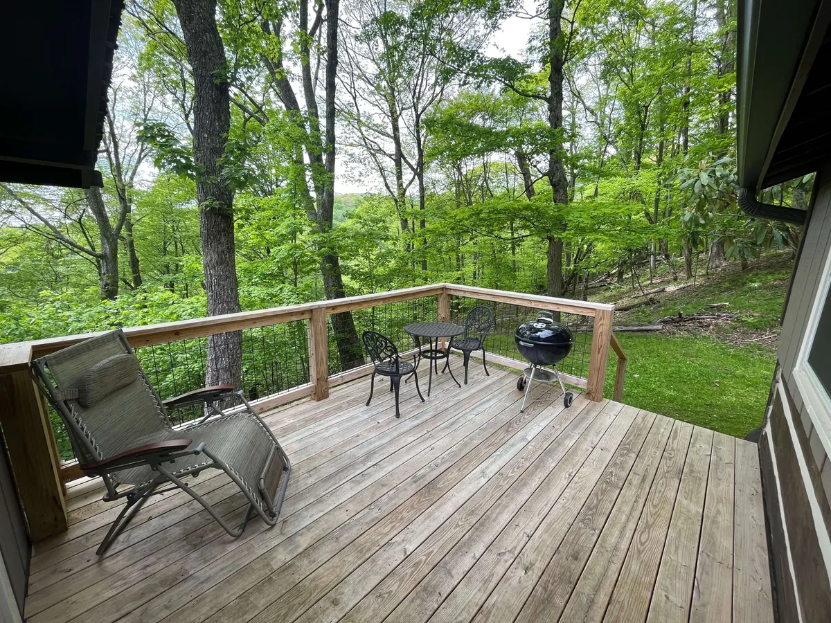 A spacious wooden deck overlooks a canopy of green trees, furnished with comfortable outdoor furniture and a grill. The serene space hints at opportunities for barbecues, family gatherings, and enjoying nature, with the deck seamlessly connecting indoor comfort to outdoor adventure.