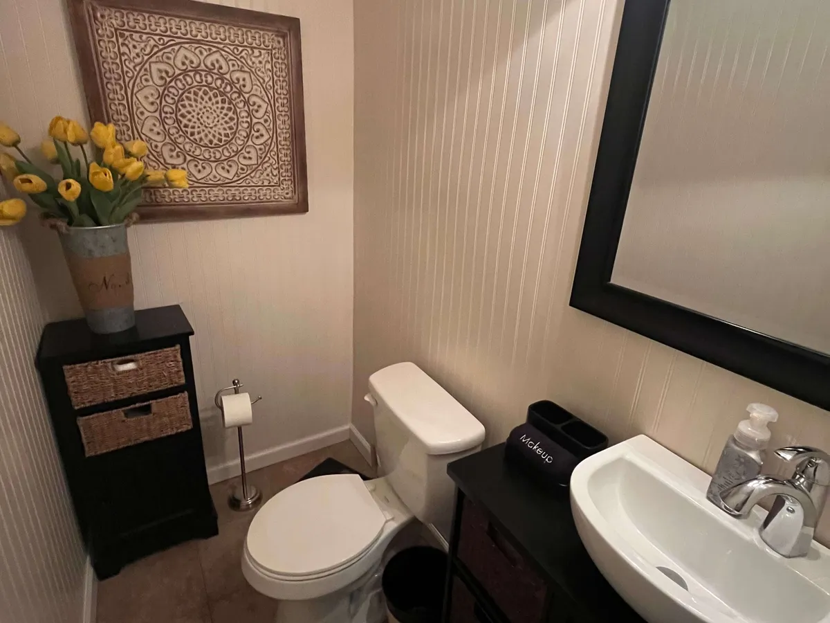 A modern, updated bathroom with a stylish sink, contemporary fixtures, a vase of yellow flowers, and tasteful wall art. The mood is calm, clean, and rejuvenating, ideal for unwinding or preparing for the day.