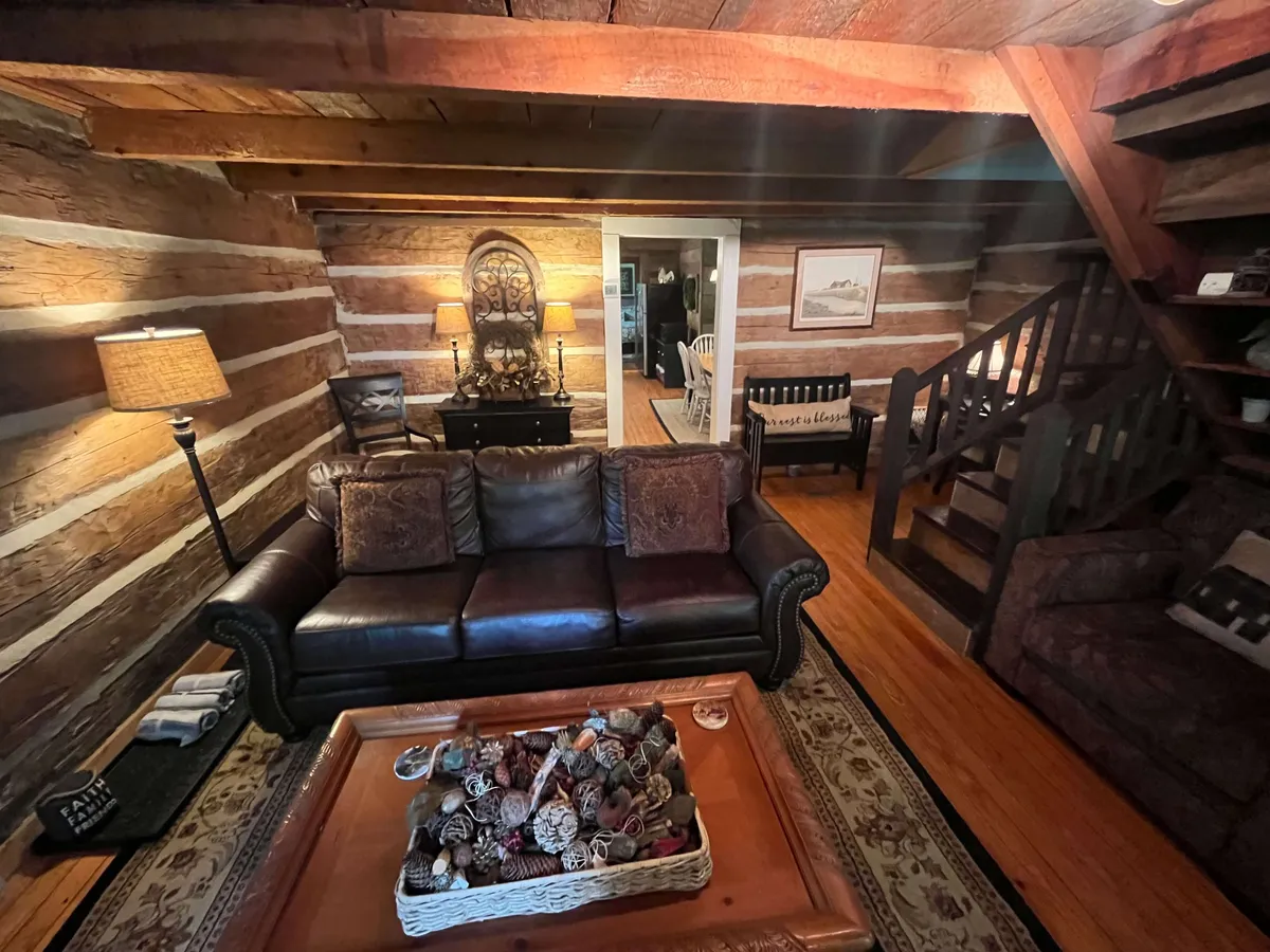 A cozy corner with a leather sofa, coffee table adorned with a decorative bowl, prominent wooden beams overhead, and soft, ambient lighting from a lamp.