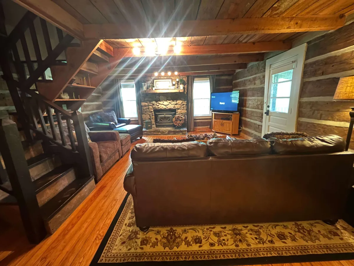 A welcoming living room features a rustic stone fireplace, a plush leather sofa, and a wooden staircase. The warm glow of the fire creates an intimate, cozy atmosphere ideal for couples seeking relaxation after exploring the mountains.