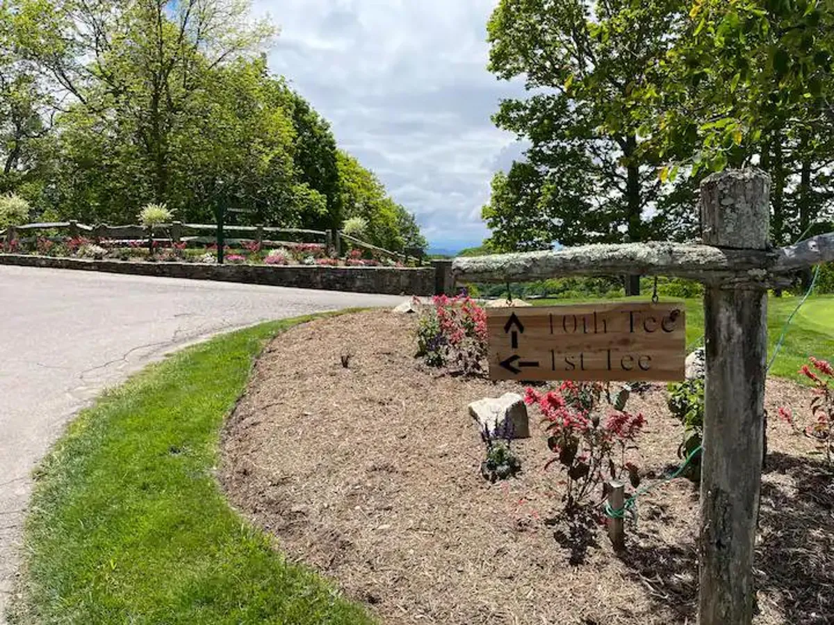 An inviting exterior featuring a wooden signpost amidst flower beds, a grassy area, and a paved pathway suggesting leisurely exploration and connection with the outdoors.
