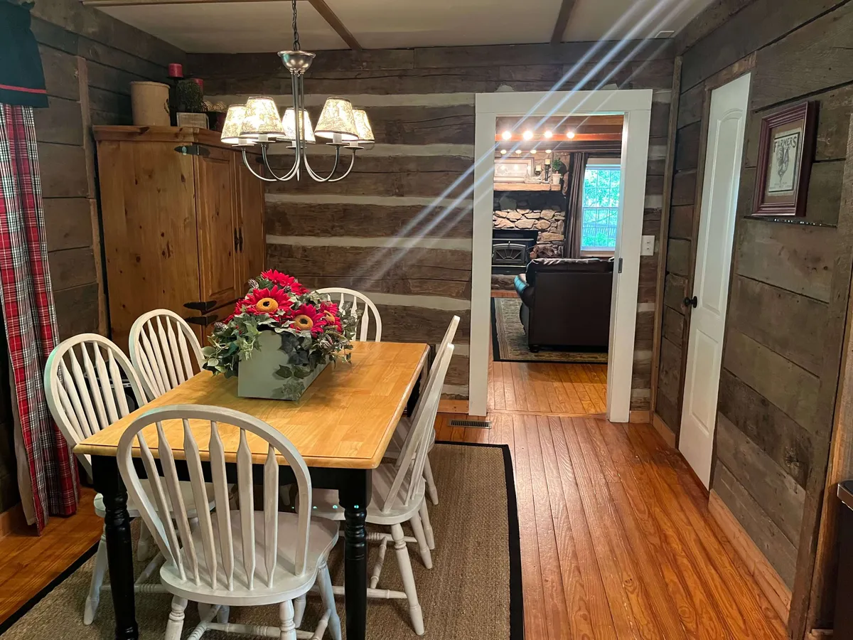 This image presents a spacious wooden dining table adorned with a floral centerpiece under a glowing chandelier, set against log cabin walls. The room feels ready for lively family meals, storytelling, and special celebrations.