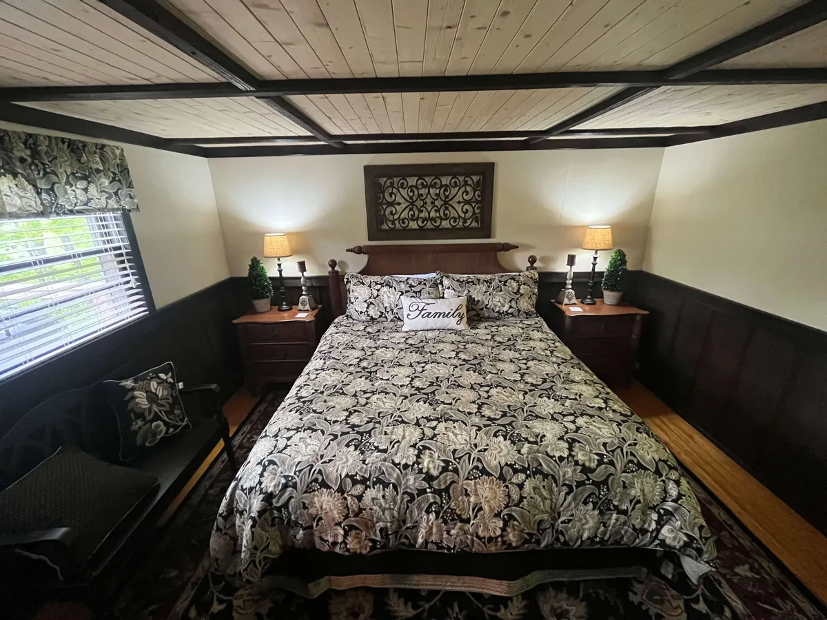 A bedroom featuring a bed with floral bedding, a decorative headboard, nightstands with lamps, and warm, welcoming lighting. The space feels inviting and personal, ideal for creating memories or unwinding after a day outdoors.