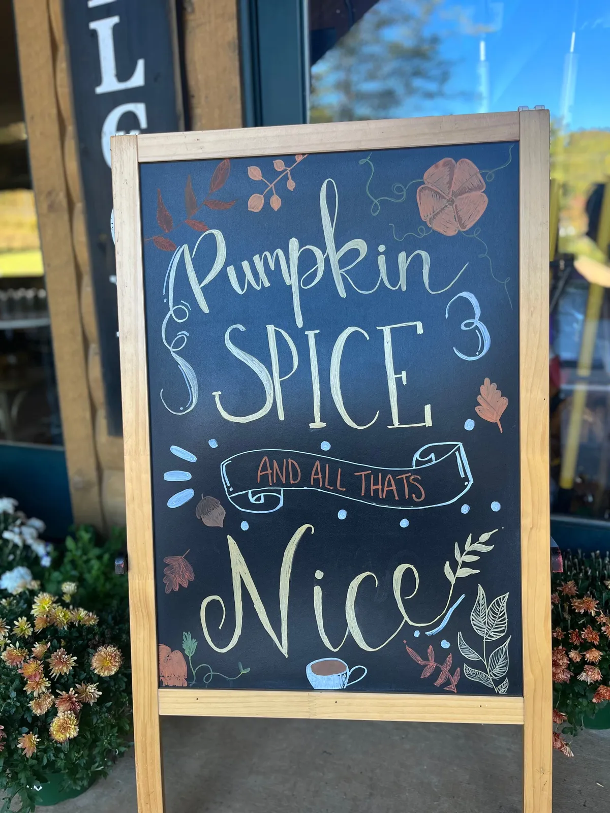 A charming exterior scene featuring a chalkboard sign welcoming visitors, vibrant flowers in the foreground, and a rustic wooden structure behind the sign, evoking a sense of community and local tradition.