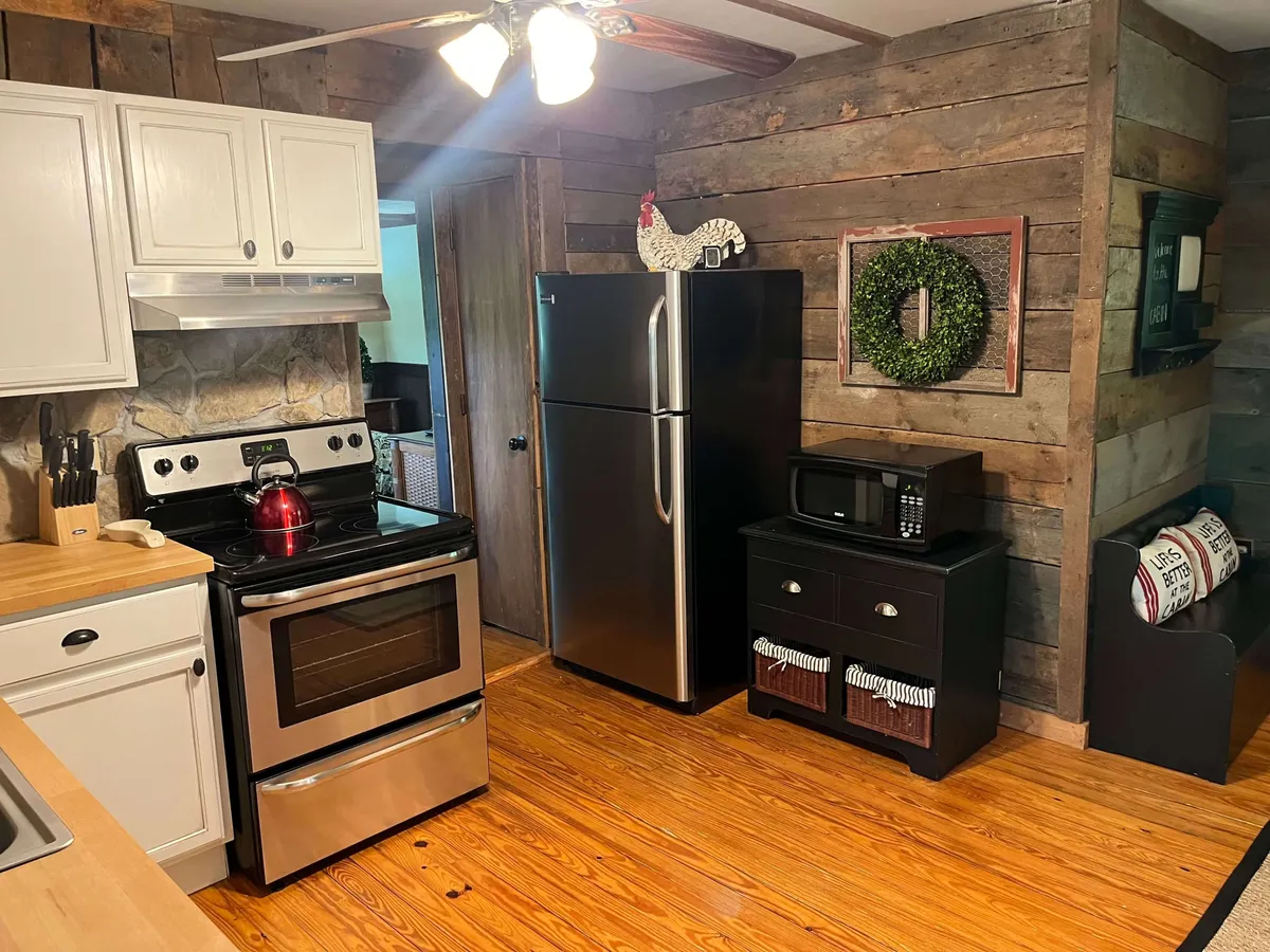 The image features a kitchen space with contemporary stainless steel appliances, a wooden countertop, a decorative rooster, and a festive wreath on the wall, creating an inviting and homey vibe. The layout hints at an open plan for easy movement between kitchen and dining.